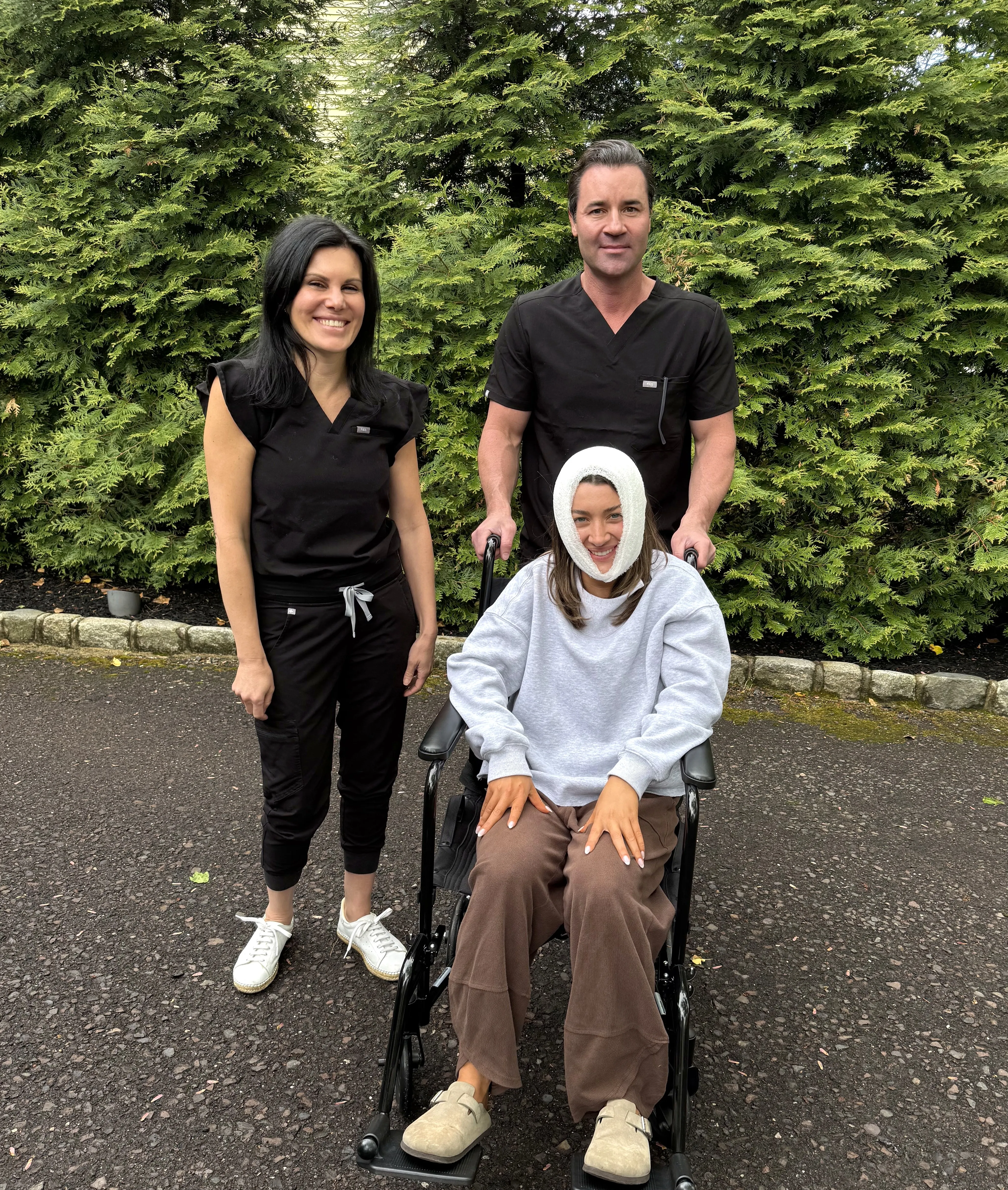 Two Prestige nurses walking a woman in a wheelchair, recovery bandage in place, up a home driveway